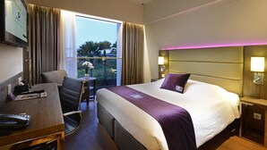 Une chambre d’hôtel avec un grand lit, un bureau avec une chaise, une petite table et une vue sur les palmiers à l’extérieur.