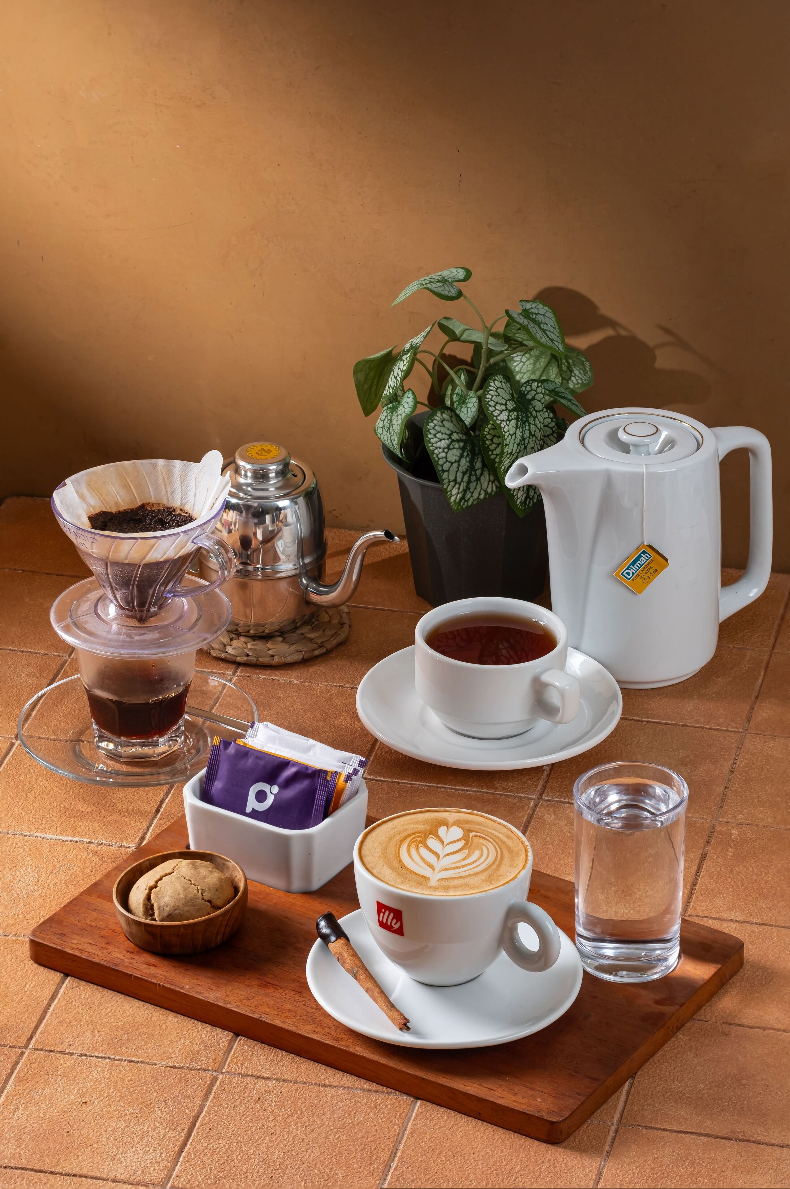 A table with a coffee setup including a coffee pot, a drip coffee maker, a cup of coffee, a glass of water, a cookie, and a box of tea bags.
