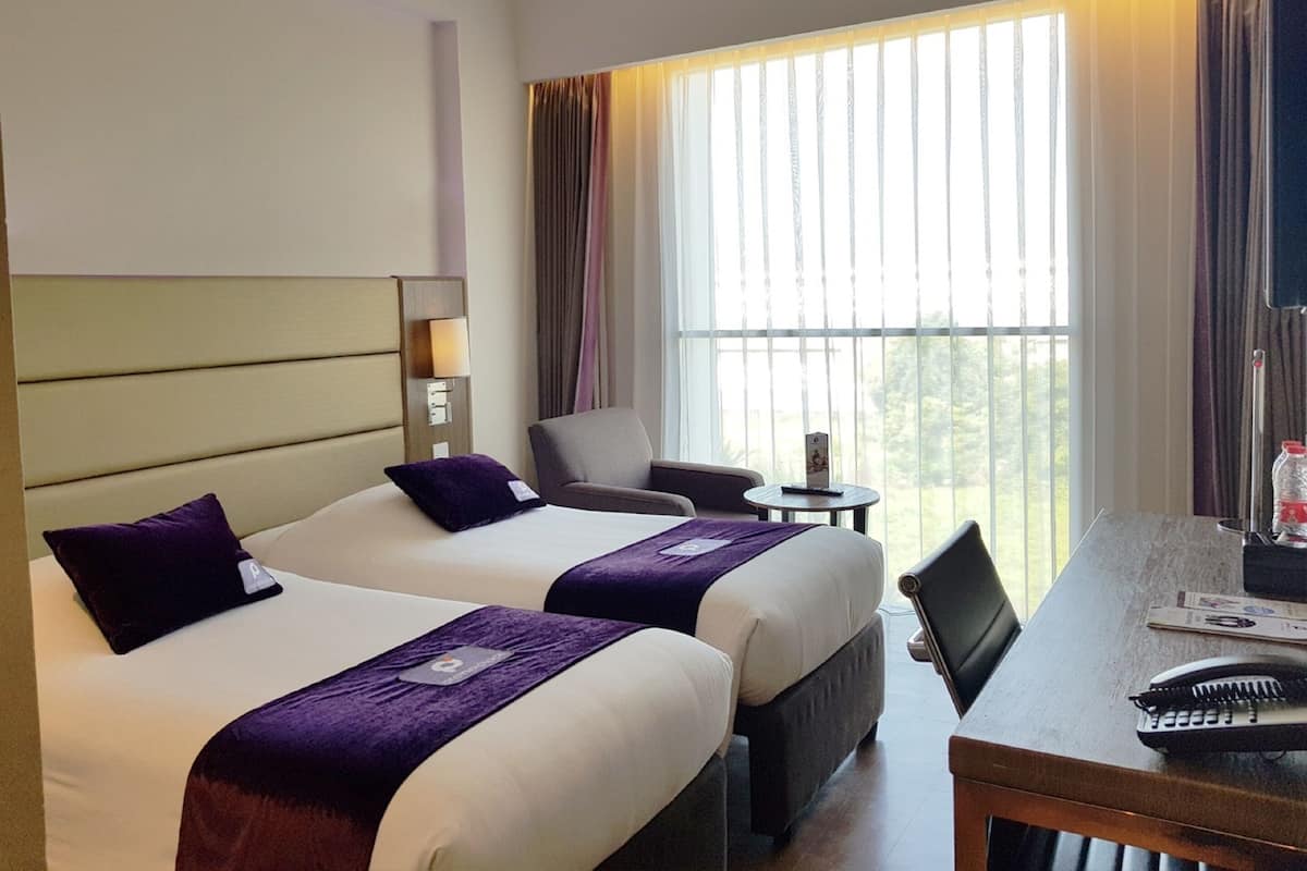 Habitación de hotel con dos camas, un escritorio, una silla y una ventana con cortinas.