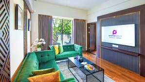Un salon moderne avec un canapé vert, une table basse et un téléviseur diffusant l’image de « Premier Place Surabaya Airport ».
