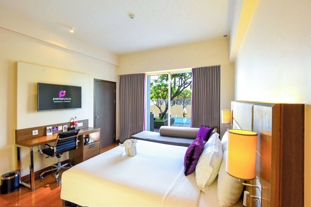Habitación de hotel con cama, escritorio, silla, televisor y vistas al exterior.