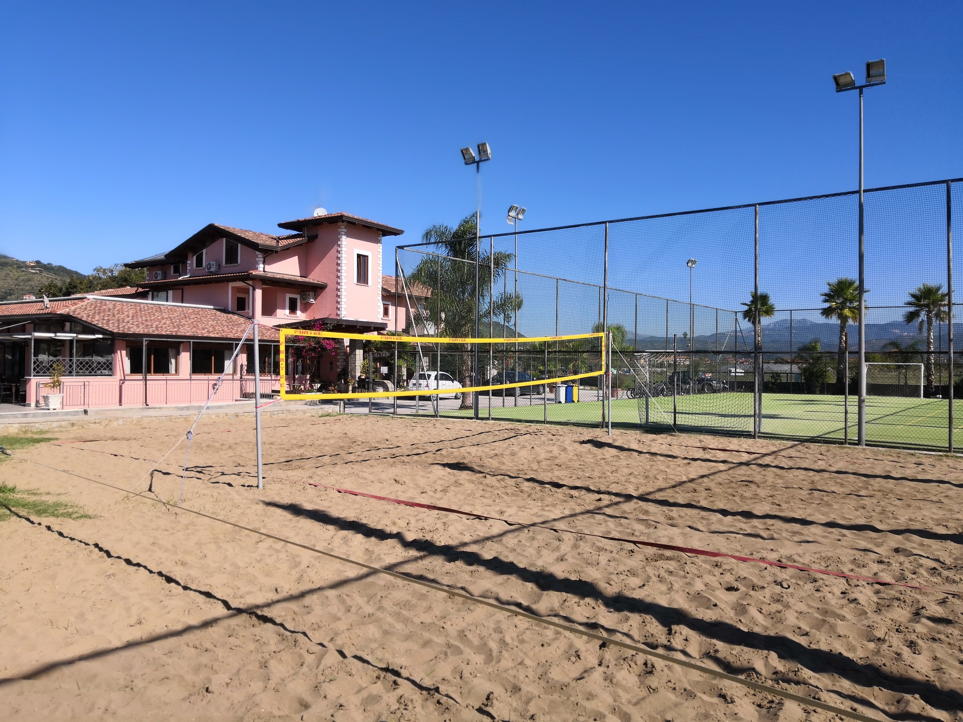 Un terrain de volley-ball avec un filet, entouré d’une clôture, et un bâtiment en arrière-plan.