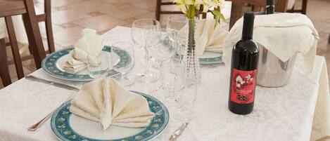 Une table à manger dressée avec des assiettes, des verres, une bouteille de vin et un vase rempli de fleurs.