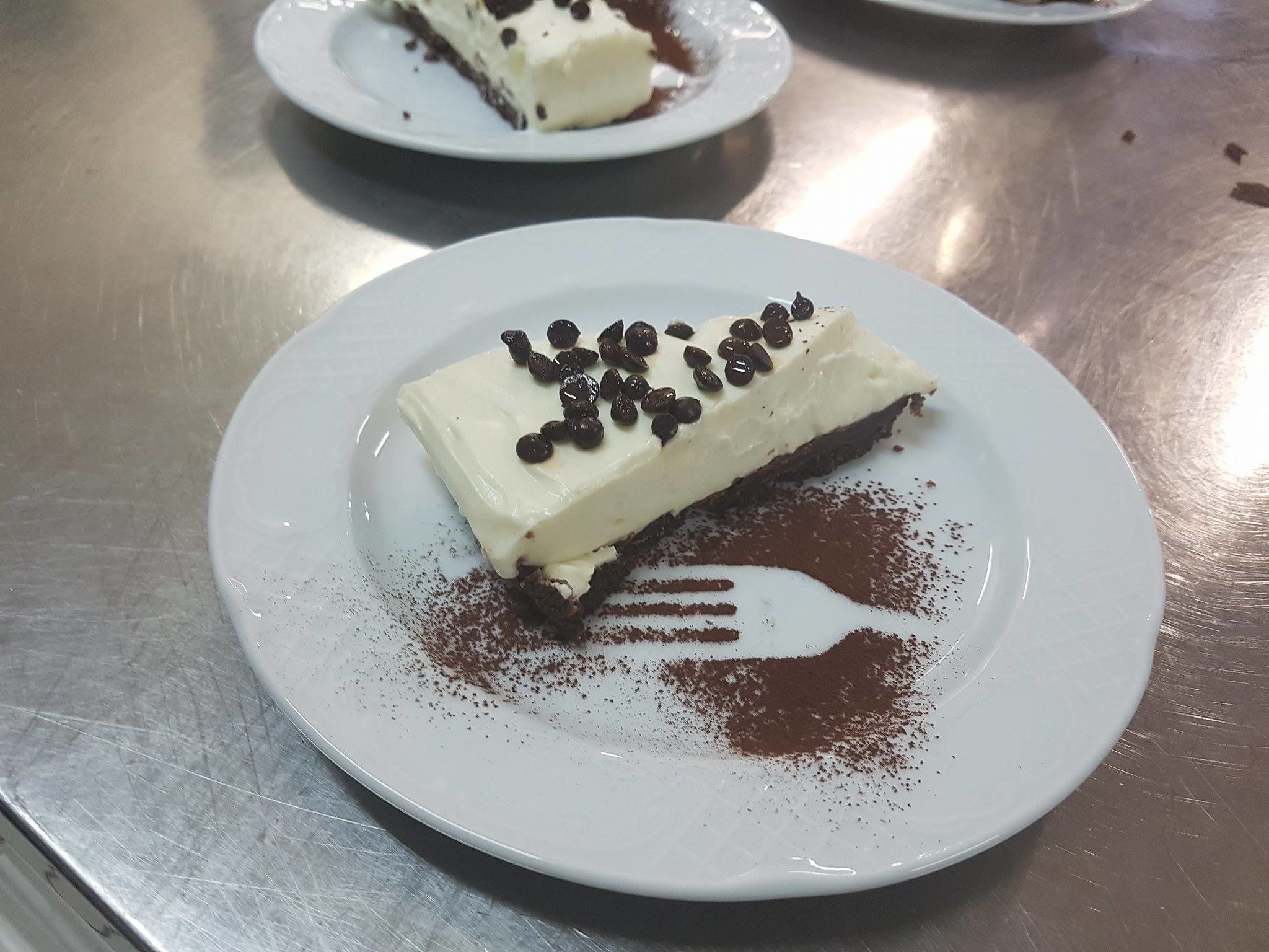 En bit dessert på en tallrik, med en gaffel bredvid, lite kakao pudrat över och chokladbitar ovanpå.