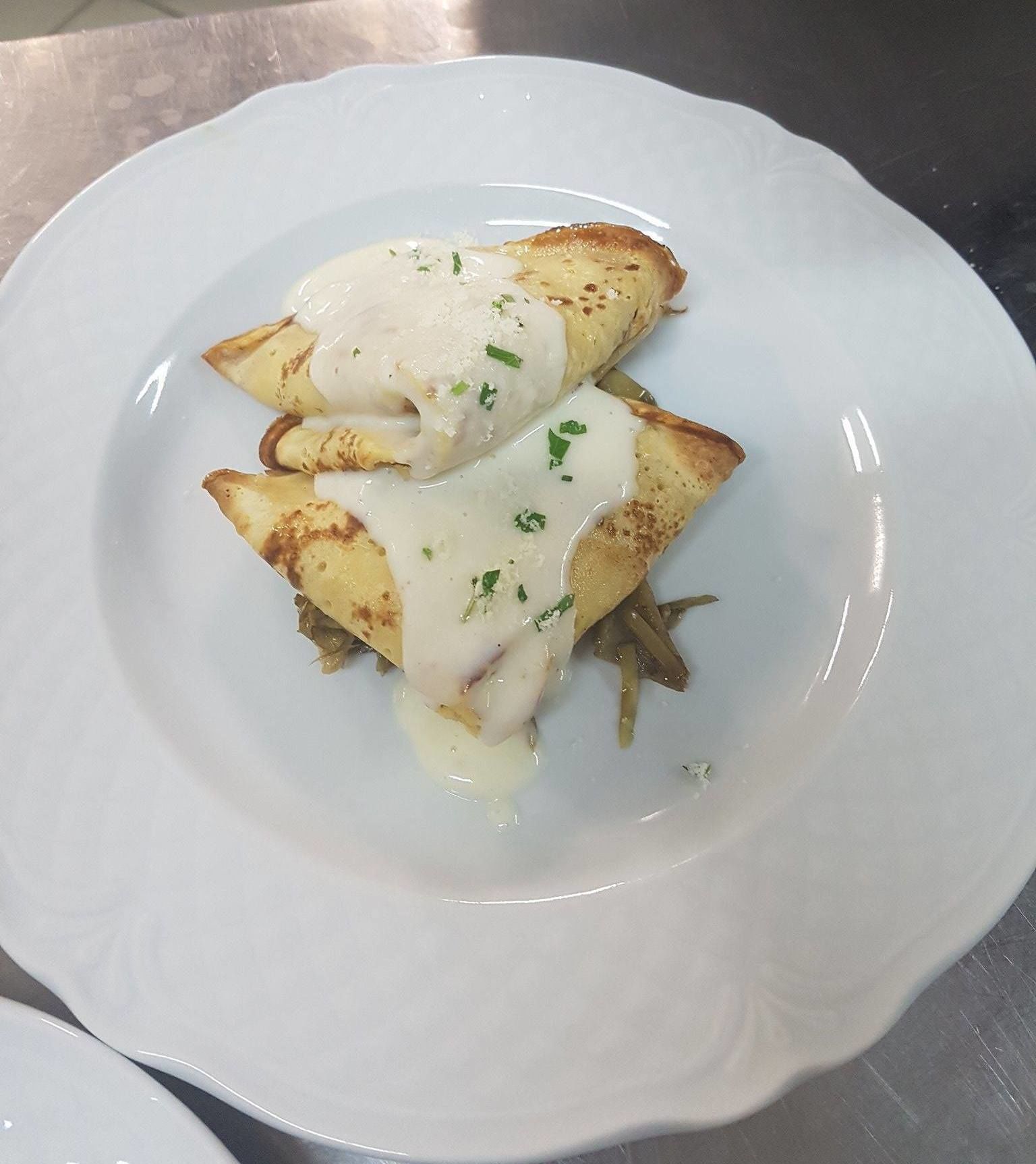 Un plato con un guiso sobre una base dorada, cubierto con salsa blanca cremosa y adornado con hierbas verdes.