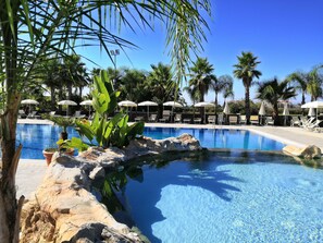 A pool with clear blue water, surrounded by palm trees and lounge chairs. - L'Oasi del Fauno Country House (Casal Velino)