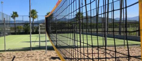 Cancha de voleibol de playa con arena, una red, una cerca y palmeras.