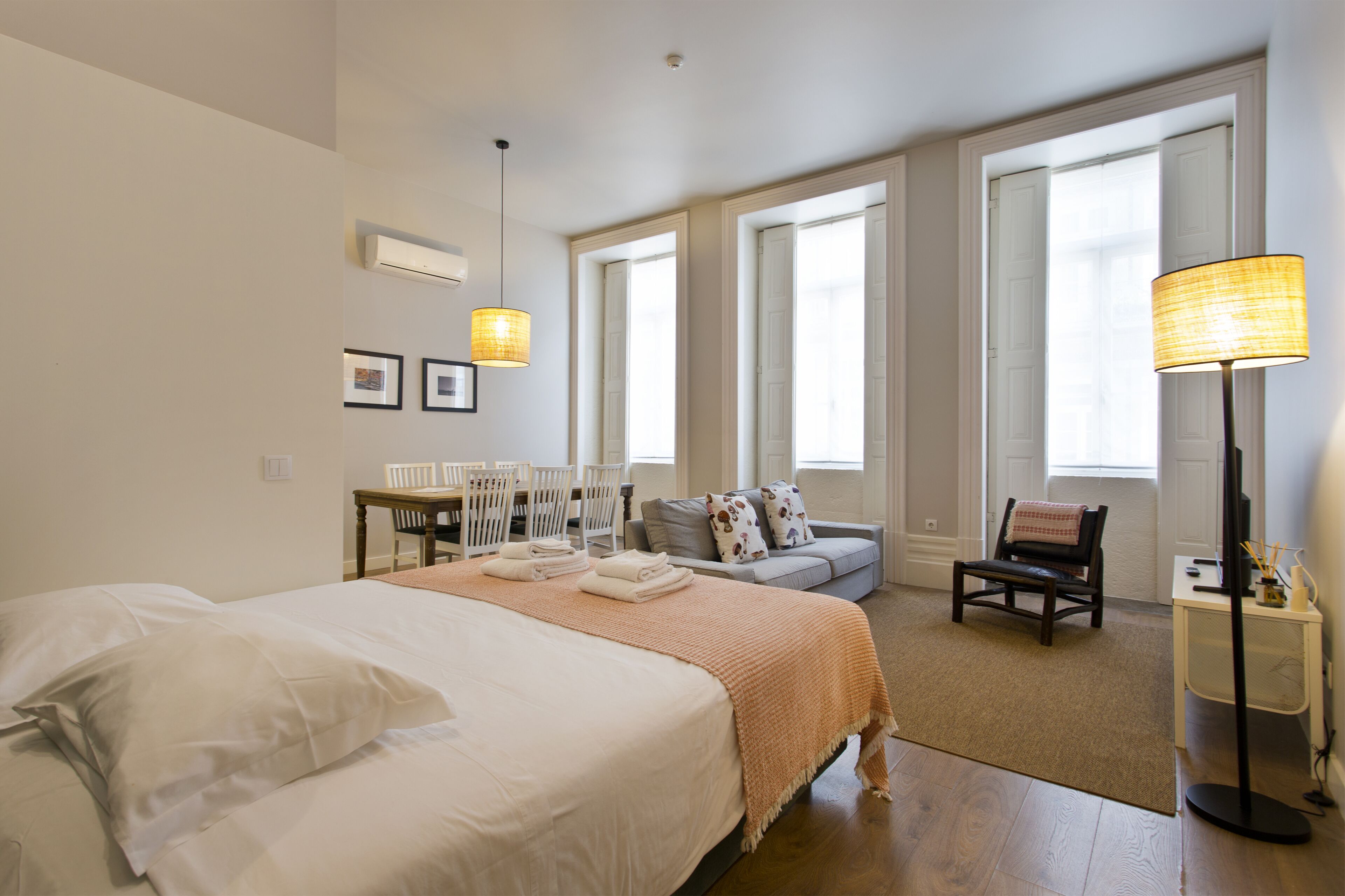 Une chambre d’hôtel avec un grand lit, un canapé, un bureau et une chaise. Elle dispose de plusieurs fenêtres qui laissent entrer la lumière naturelle.