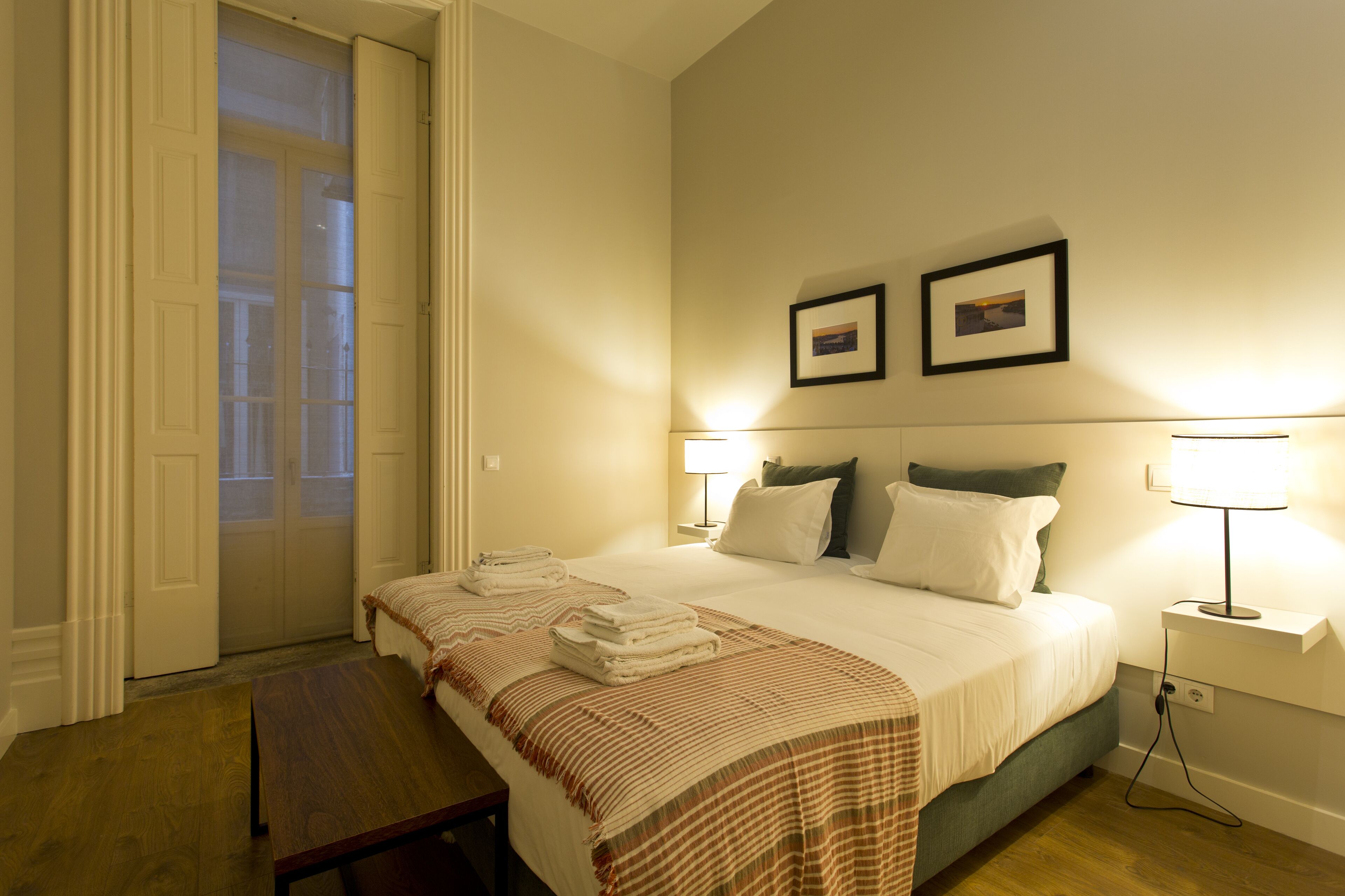 A hotel room with a bed, two bedside lamps, a framed picture on the wall, and a door leading to the outside.
