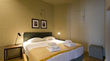 A hotel room with a bed, bedside table, lamp, and a small stool.