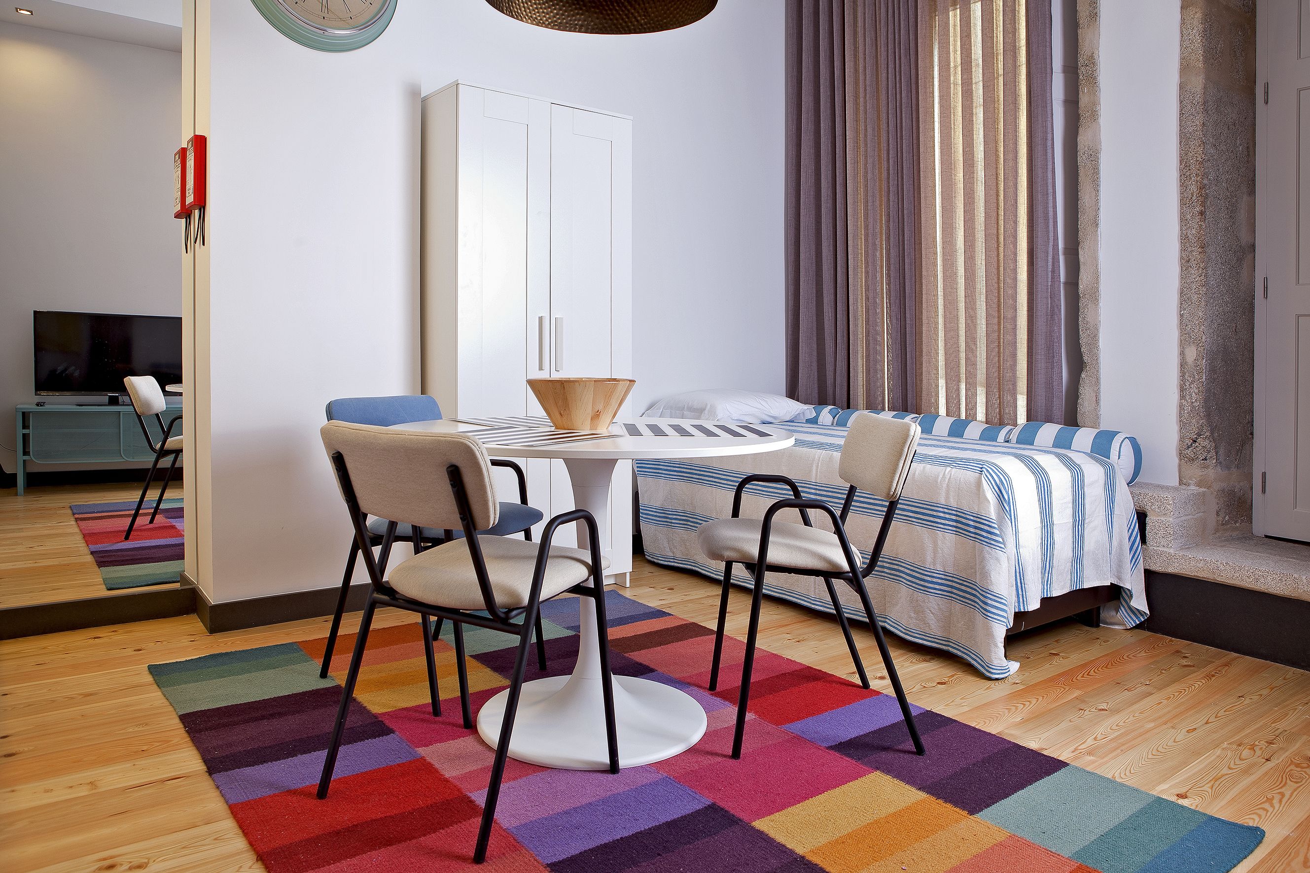 A modern bedroom with a bed, bedside table, and a chair. There is a small table with a chair in the corner.