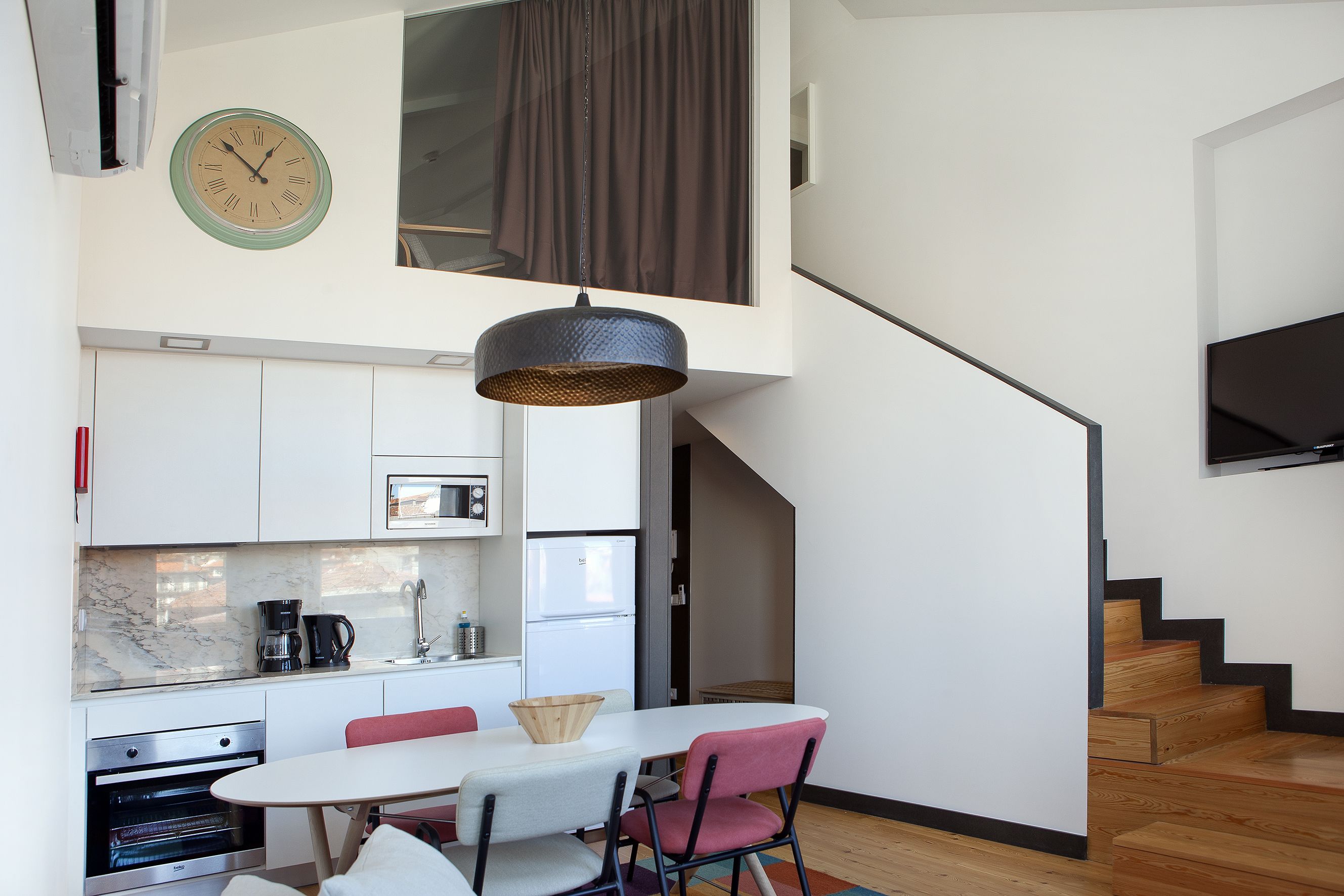 Une cuisine moderne avec un coin repas, une horloge et un escalier.