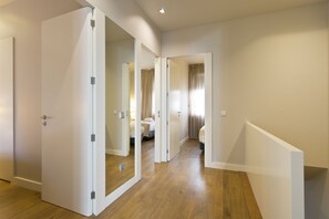 A modern hotel room with a wooden floor, a large mirror, and a bed with a headboard.