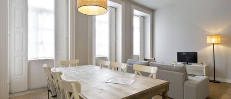 A dining area with a wooden table and chairs, a sofa, a television, and a floor lamp.