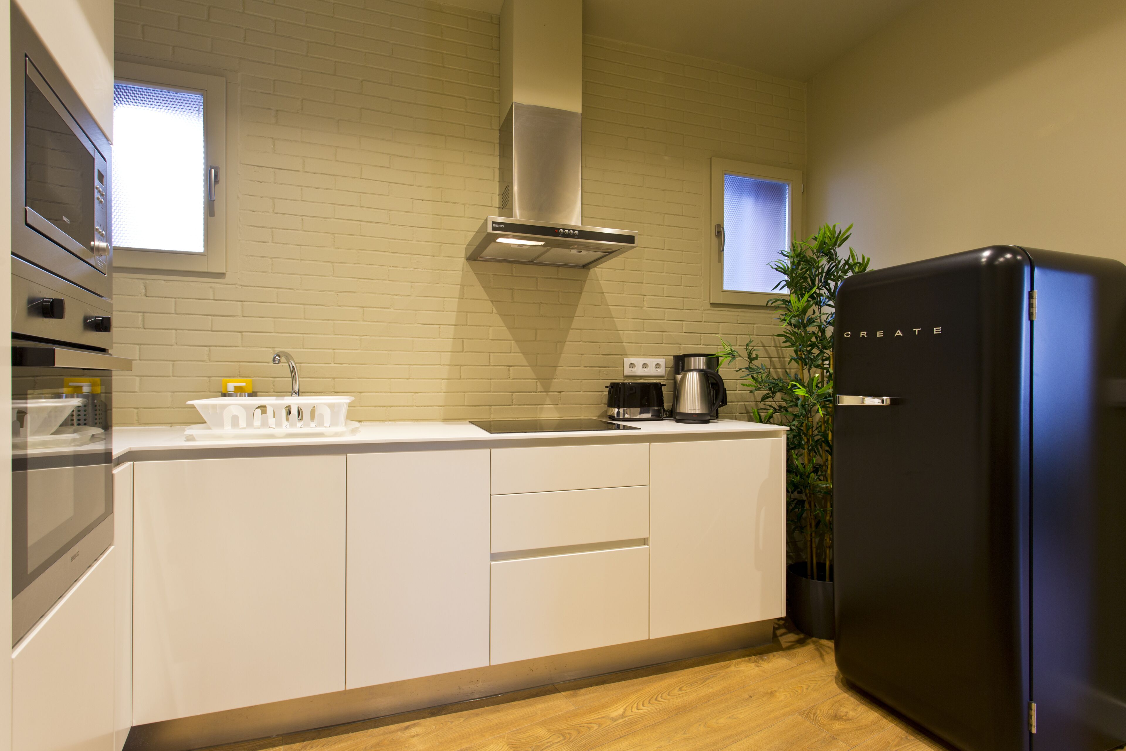 Eine moderne Küche mit weißen Schränken, einer Edelstahl-Dunstabzugshaube, einem schwarzen Kühlschrank und einer Kaffeemaschine.