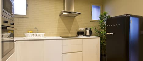 A modern kitchen with white cabinetry, a stainless steel range hood, a black refrigerator, and a coffee maker.