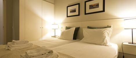 A hotel room with two beds, a large wardrobe, and two wall-mounted pictures.