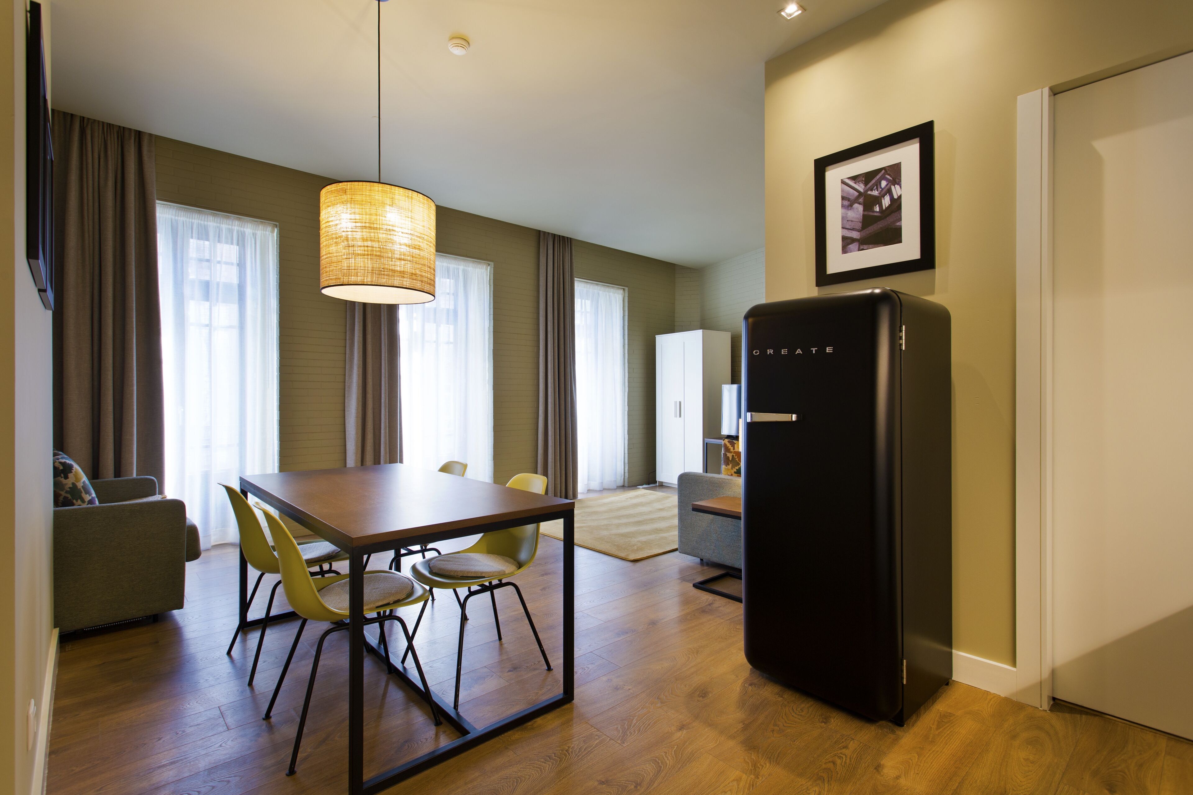 A modern kitchen with a dining table, chairs, a refrigerator, and a hanging light fixture.