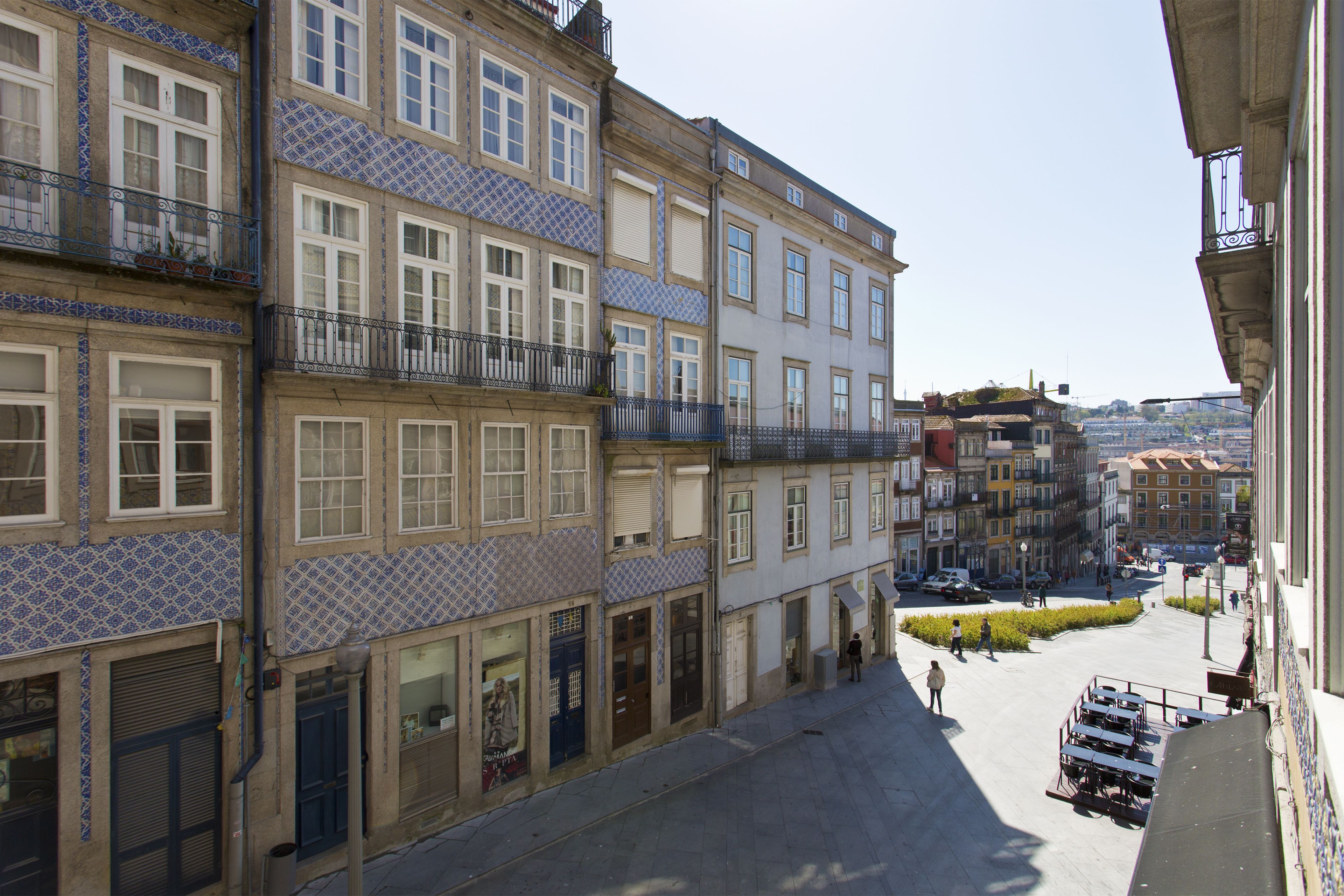 Une rue étroite bordée d’immeubles à plusieurs étages, de balcons et sous un ciel dégagé.