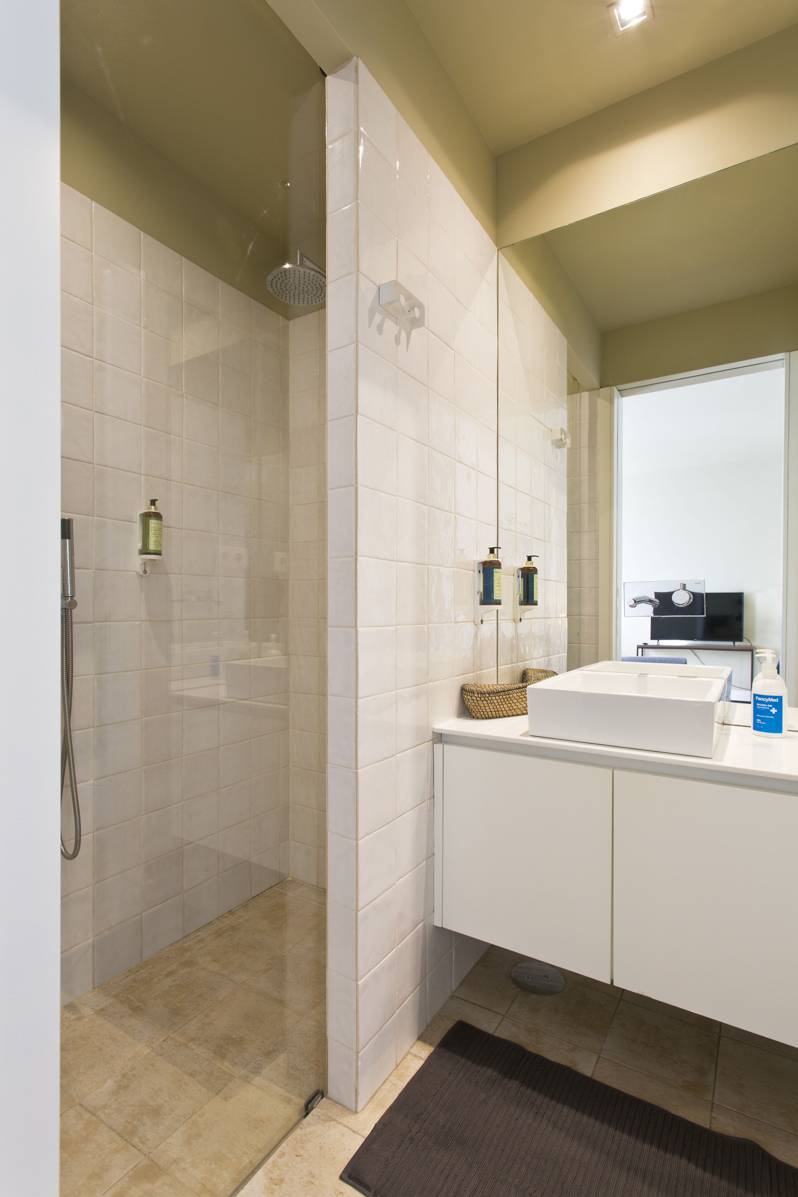 Un bagno moderno con doccia vetrata, piastrelle bianche, un lavandino bianco e uno specchio sopra il lavandino.
