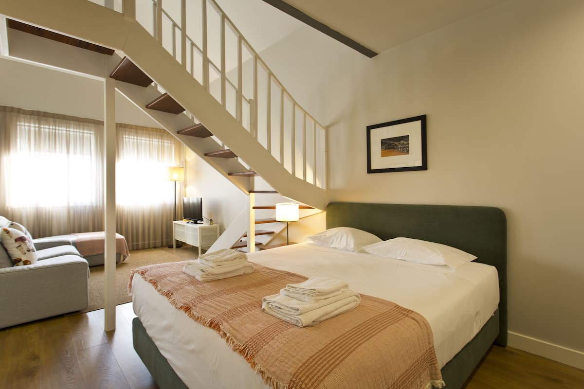 A hotel room with a bed, a sofa, a desk, and a staircase.