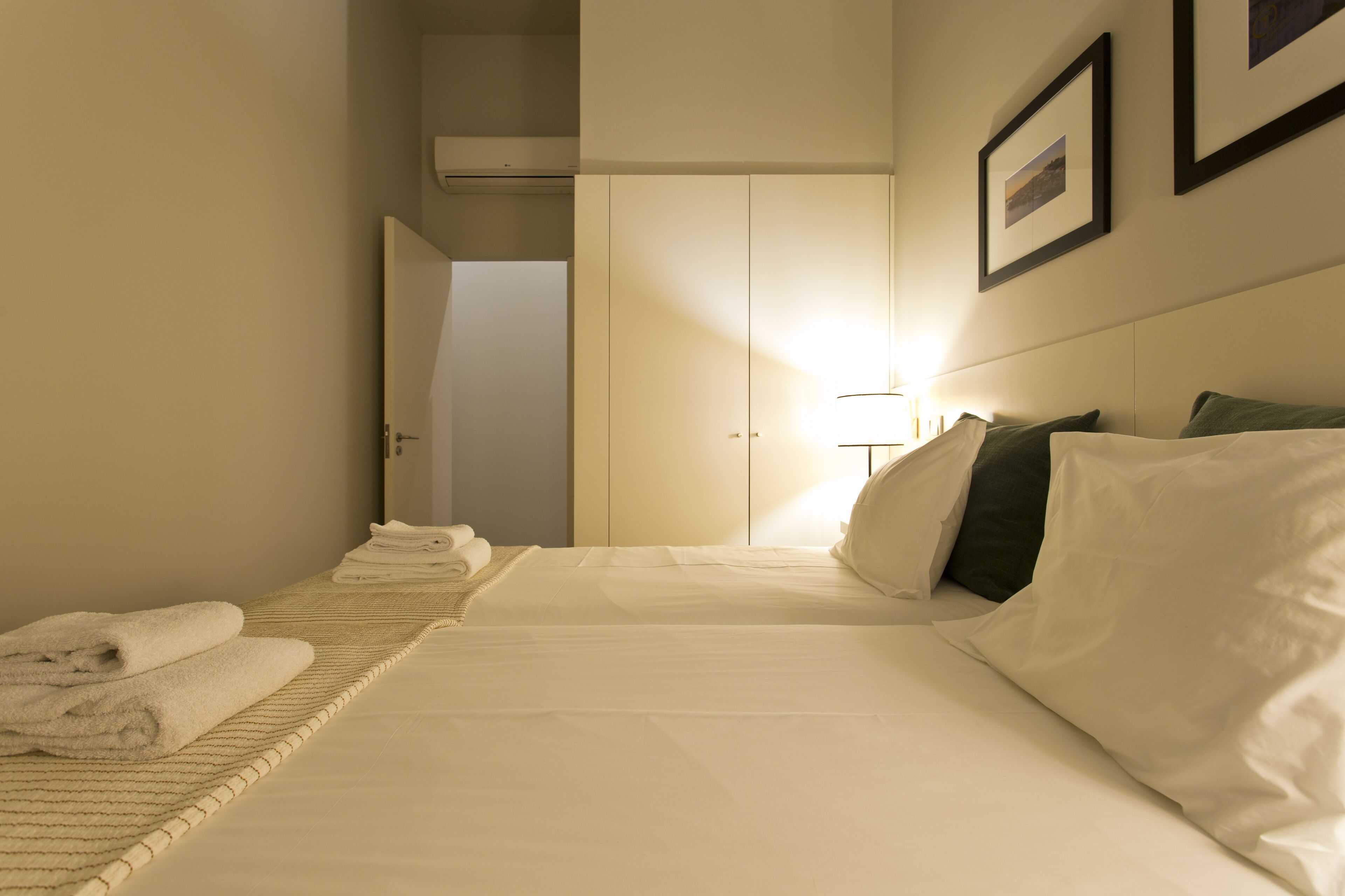 A hotel room with a neatly made bed, a bedside table, and a door leading to another room.