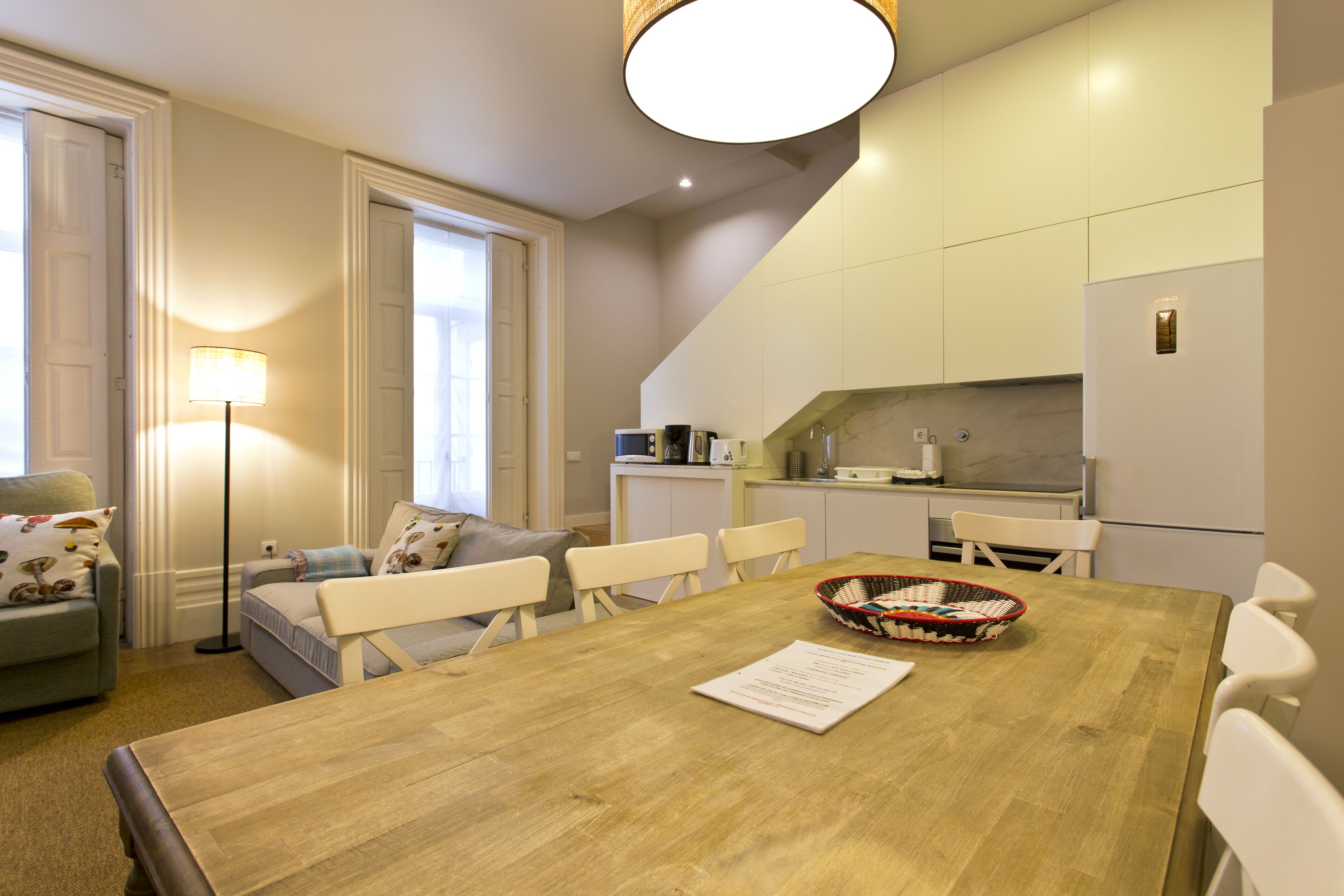 A dining area with a wooden table, white chairs, a basket, and a lamp.
