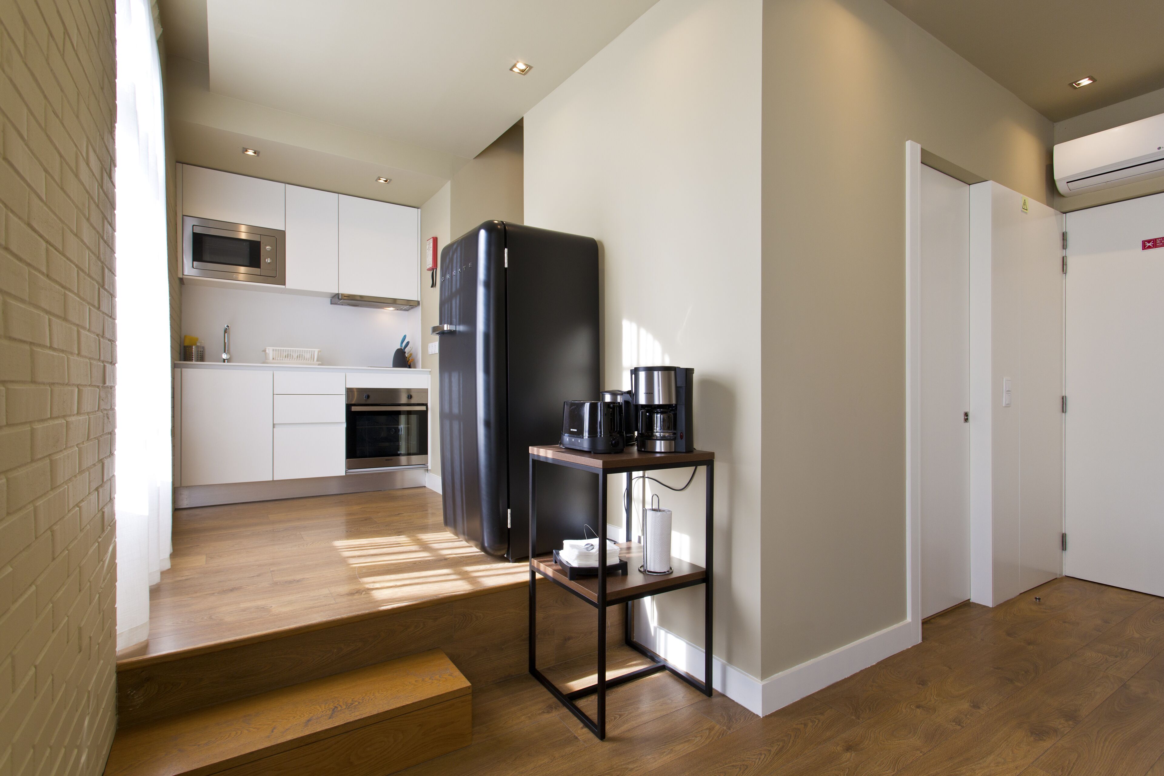 A modern kitchen with a refrigerator, microwave, and coffee maker on a shelf.