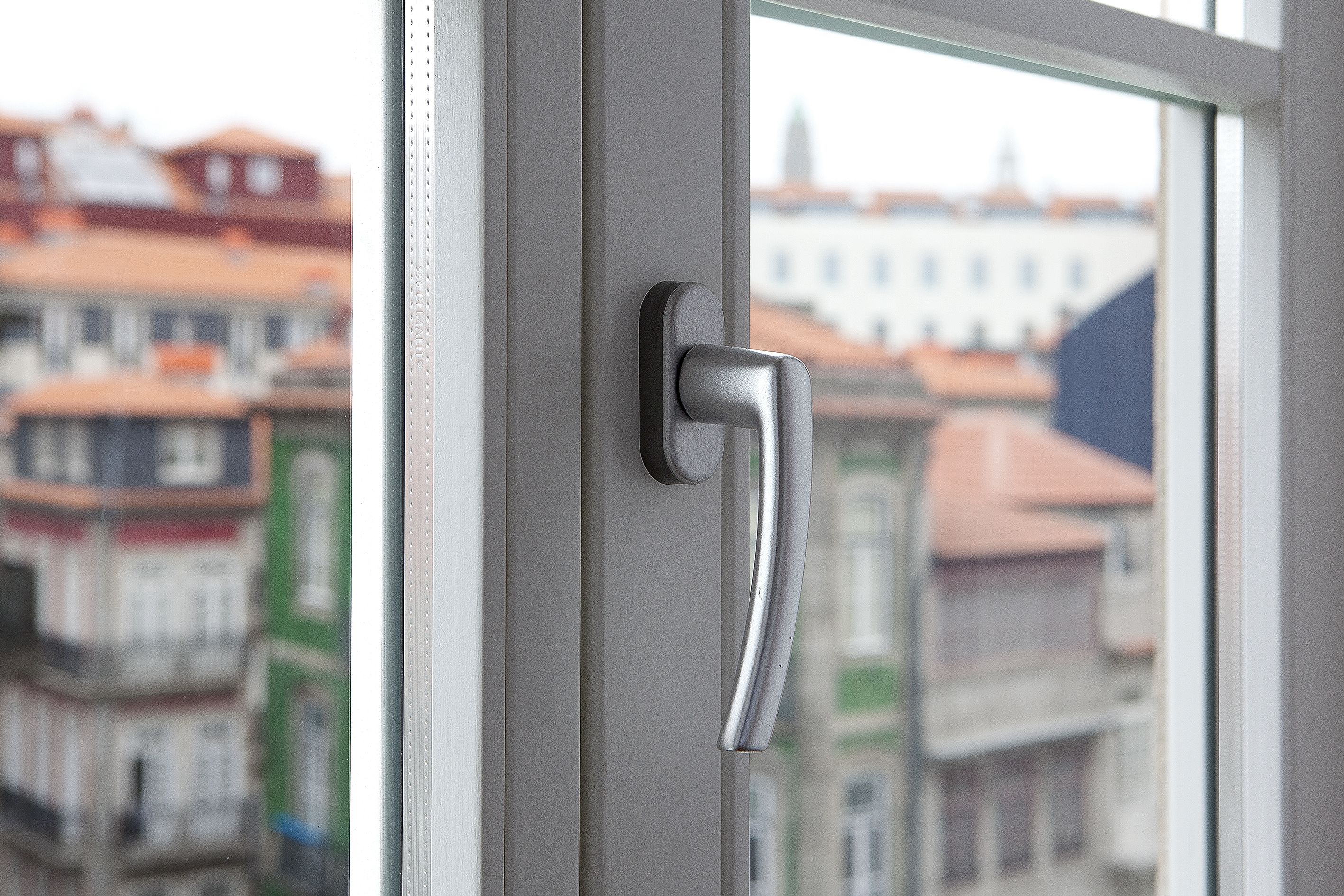 Maniglia di una porta e stipite di una finestra con vista sugli edifici circostanti.