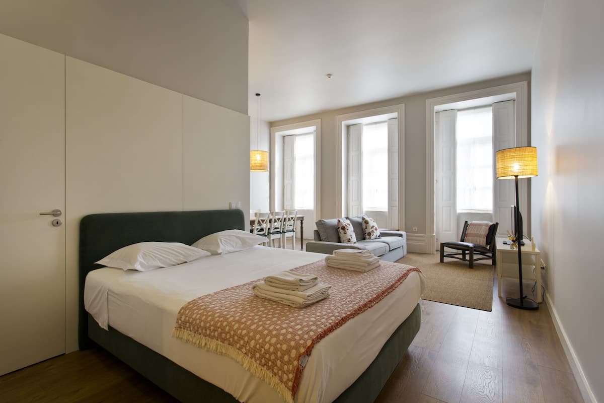 A well-lit bedroom with a large bed, a desk, and a chair.