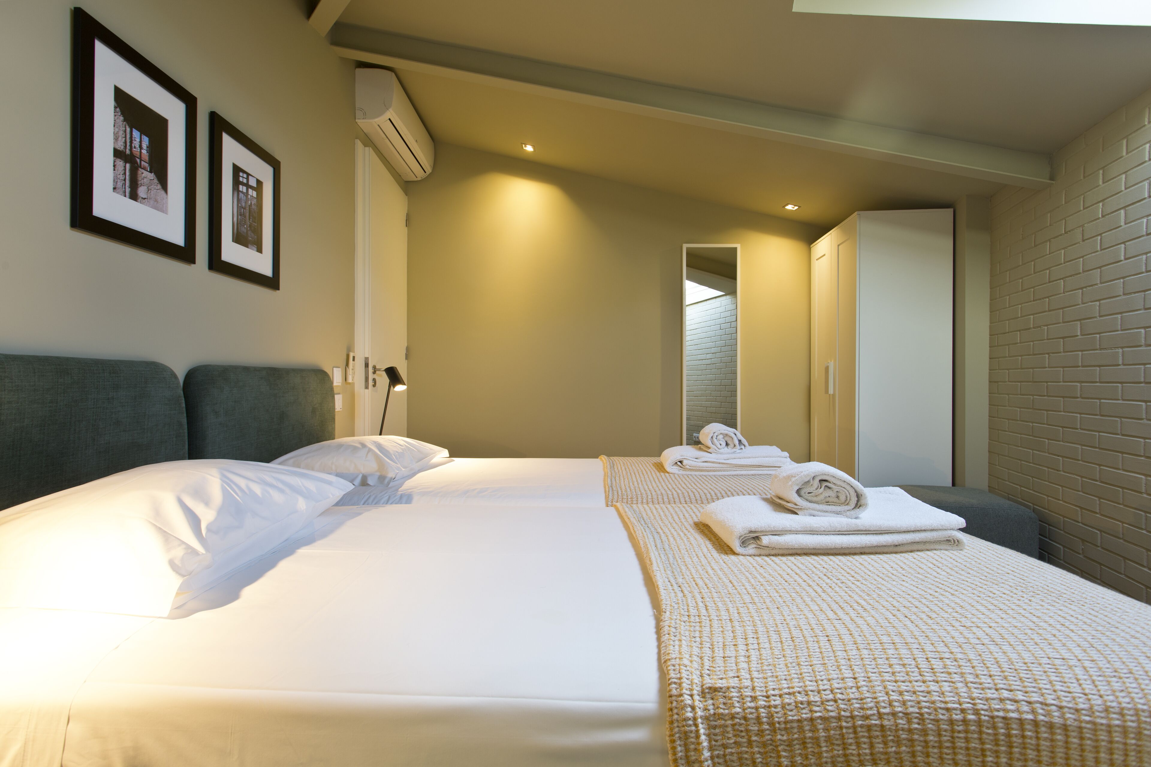 Een hotelkamer met twee bedden, een grote spiegel en een bakstenen muur.