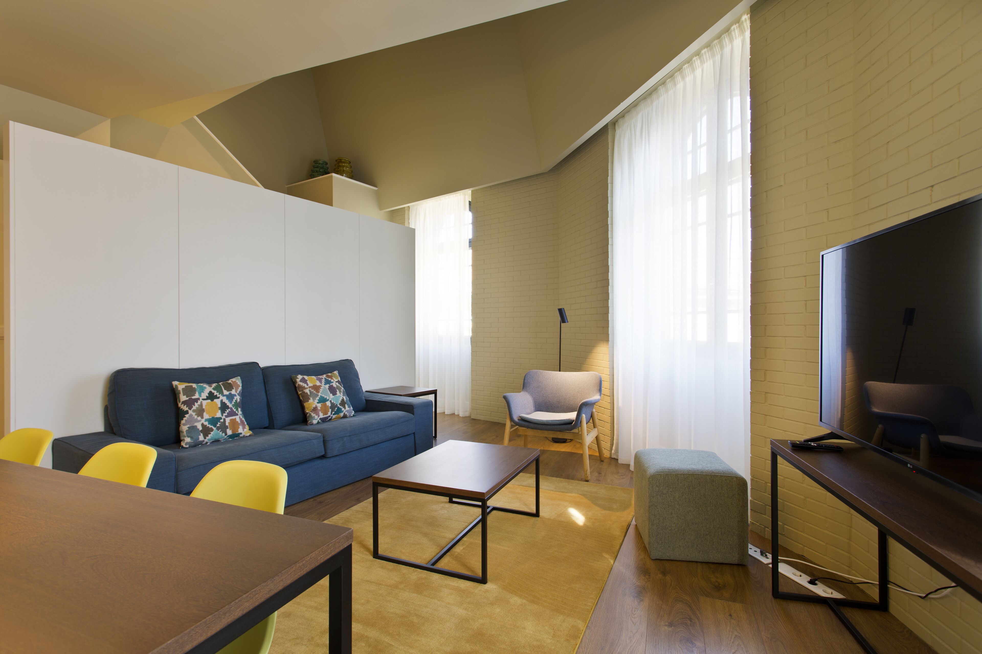 A modern living room with a sofa, chairs, a coffee table, a TV, and a brick wall.