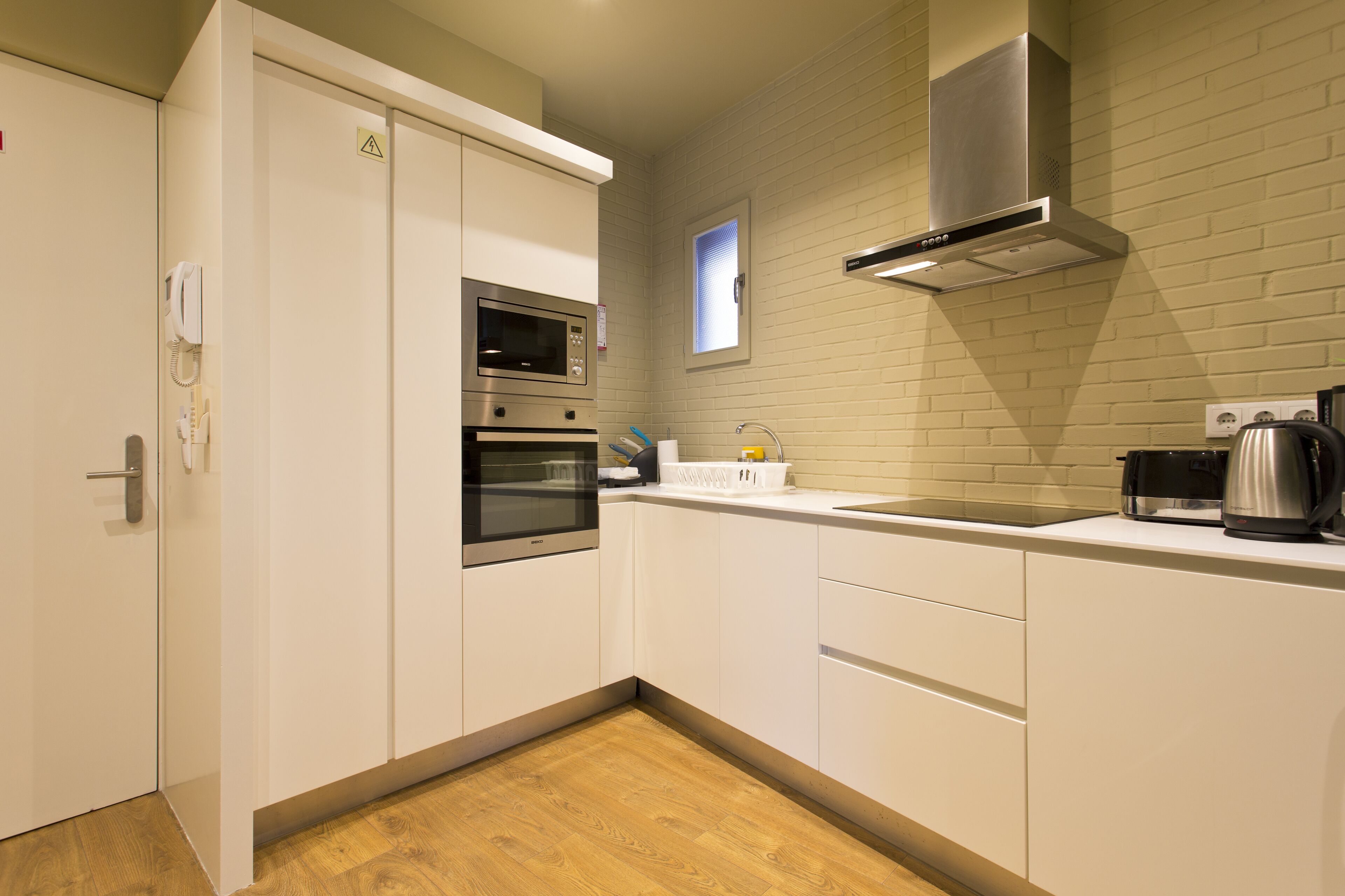 A modern kitchen with white cabinetry, a stainless steel range hood, a microwave, and a coffee maker.