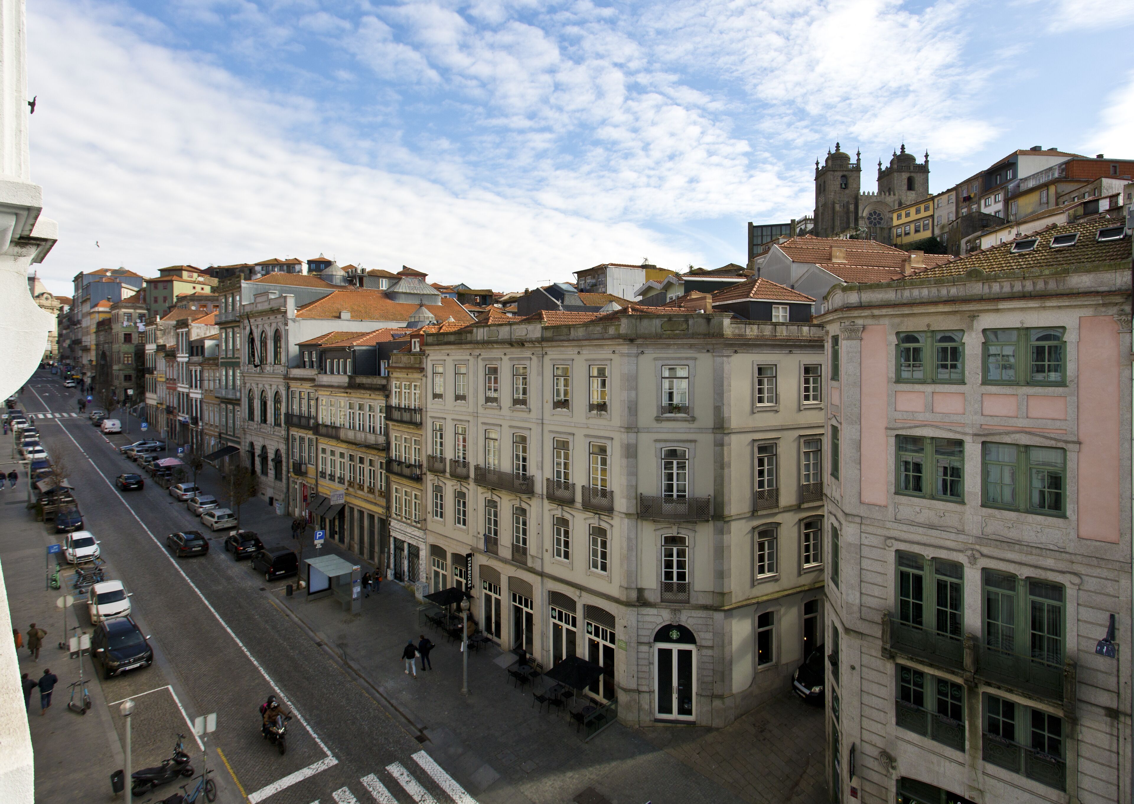 Vista de una calle en una ciudad histórica, con arquitectura tradicional, cielo despejado y coches estacionados a lo largo de la vía.