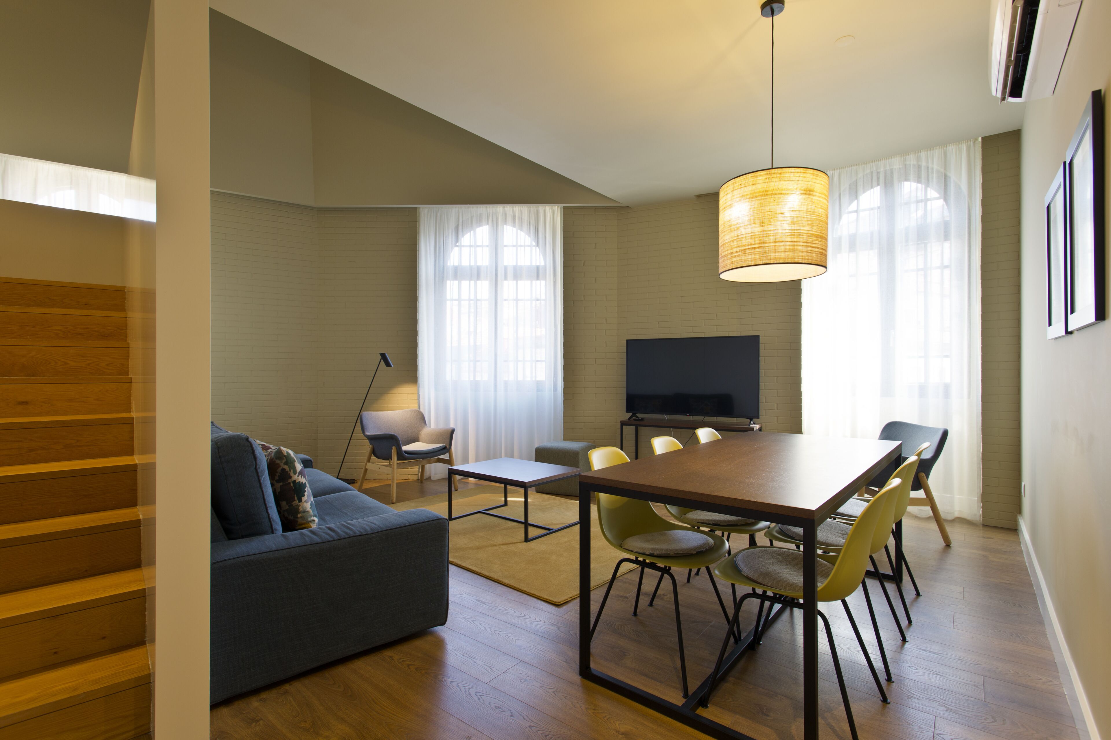 A modern living room with a sofa, dining table, chairs, and a TV.