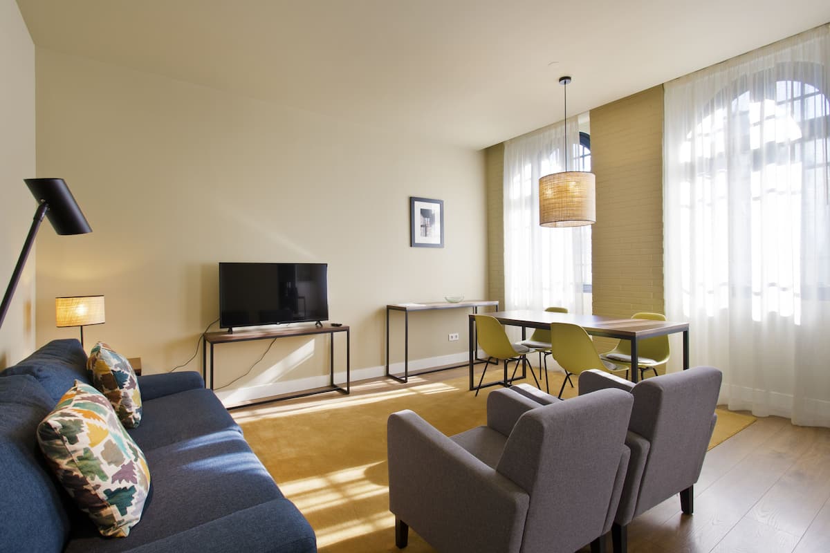 A modern living room with a sofa, chairs, a TV, a desk, and a dining area.