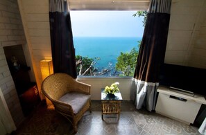 A room with a view of the ocean, a wicker chair, a small table with a vase, and a TV on a cabinet. - Shalai - The Cliff Resort (Vagator)