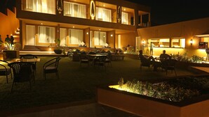 Un hotel con aree salotto all'aperto, diversi tavoli da pranzo e un ingresso ben illuminato.