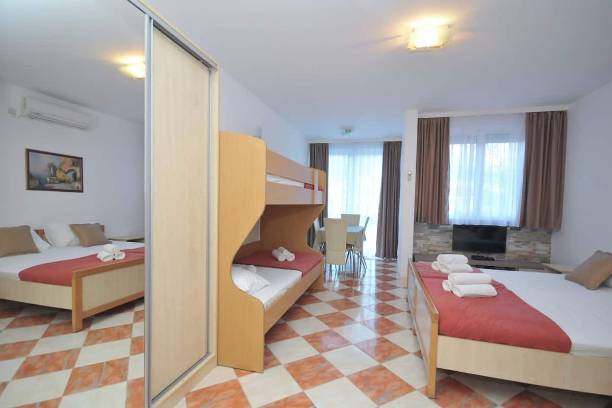 A hotel room with two beds, a sofa bed, a TV, a dining table, and a painting on the wall.