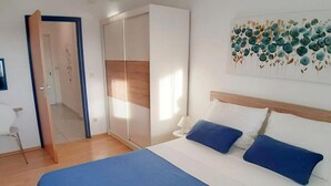 Un dormitorio con cama, armario, silla y un cuadro en la pared.