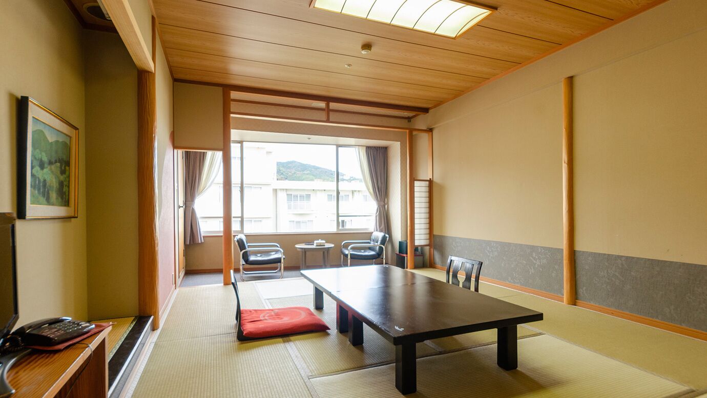 A traditional Japanese room with tatami flooring, a low table, chairs, and a view through a sliding door.