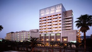 Un hotel de varios pisos con balcones, fachada de vidrio y palmeras al frente.