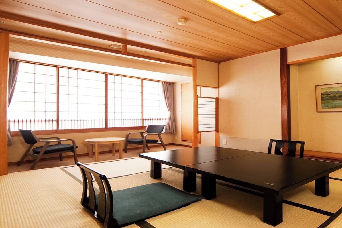 Um quarto japonês tradicional com tatames, uma mesa baixa, cadeiras, uma televisão e um quadro na parede.