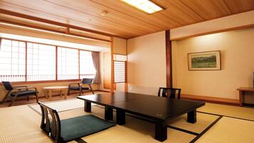 A traditional Japanese room with tatami flooring, a low table, chairs, a television, and a painting on the wall.