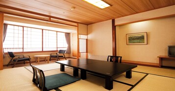 A traditional Japanese room with tatami flooring, a low table, chairs, a television, and a painting on the wall.