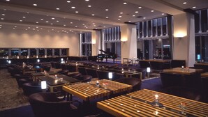 Un restaurante amplio con varias mesas y sillas, ventanas grandes y un piano al fondo.
