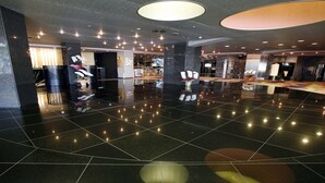 Un vestíbulo amplio con piso negro pulido, un mostrador de recepción y un área de estar con un jarrón de flores.