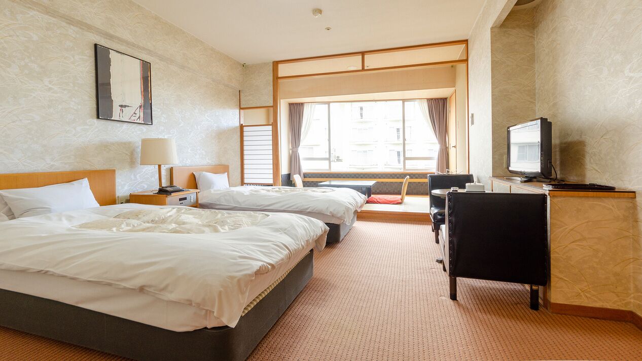 A hotel room with two beds, a desk, a television, and a window with curtains.