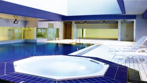 Una piscina interior con jacuzzi, paredes de azulejos y tragaluces.
