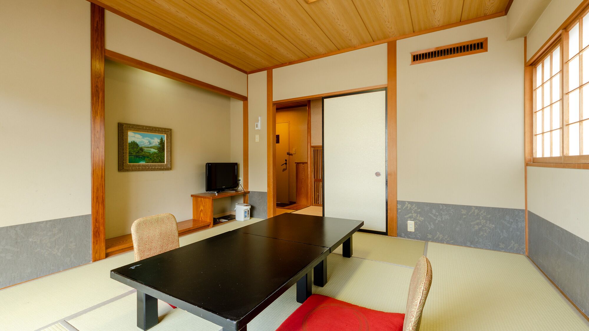 Une pièce traditionnelle avec tatamis, comprenant une petite table, des chaises, un téléviseur et un tableau accroché au mur.